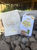 A small cream fabric drawstring pouch and a hanging card package labeled Wild Wander Cards, placed on gray stones outdoors near a weathered log.