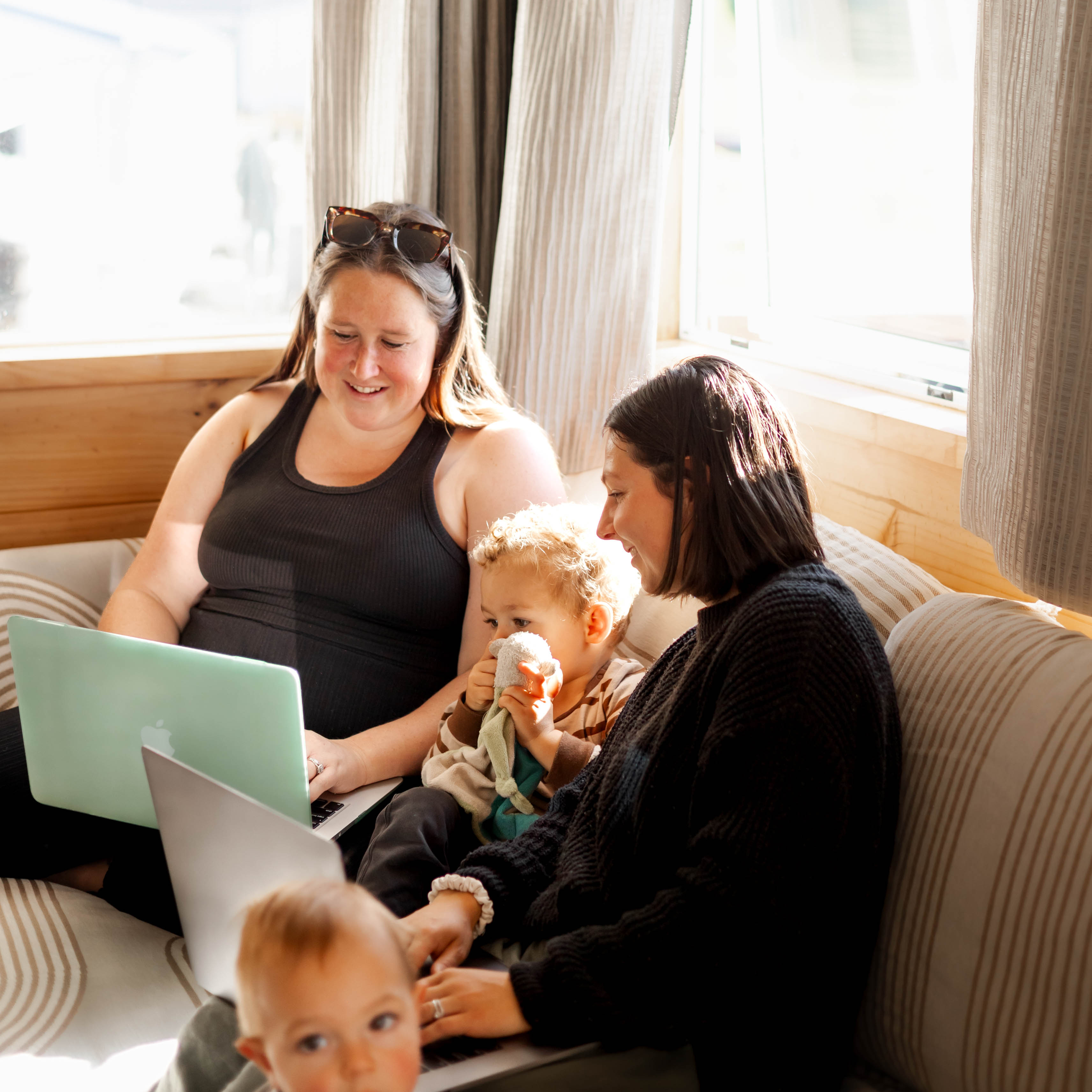 Two women sitting on a couch with two children, using a laptop.