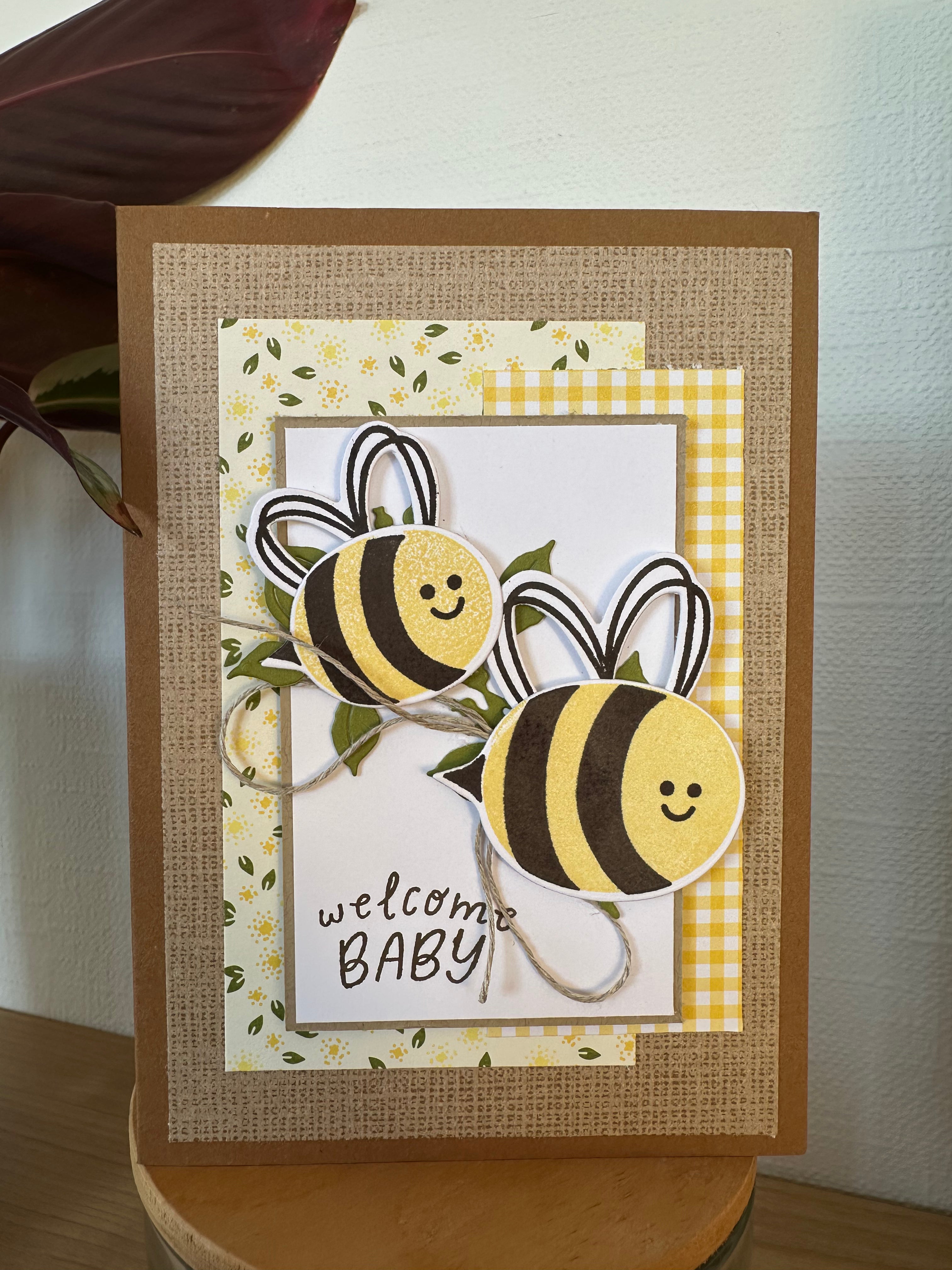 Greeting card with bee designs and 'welcome baby' text on a checkered background