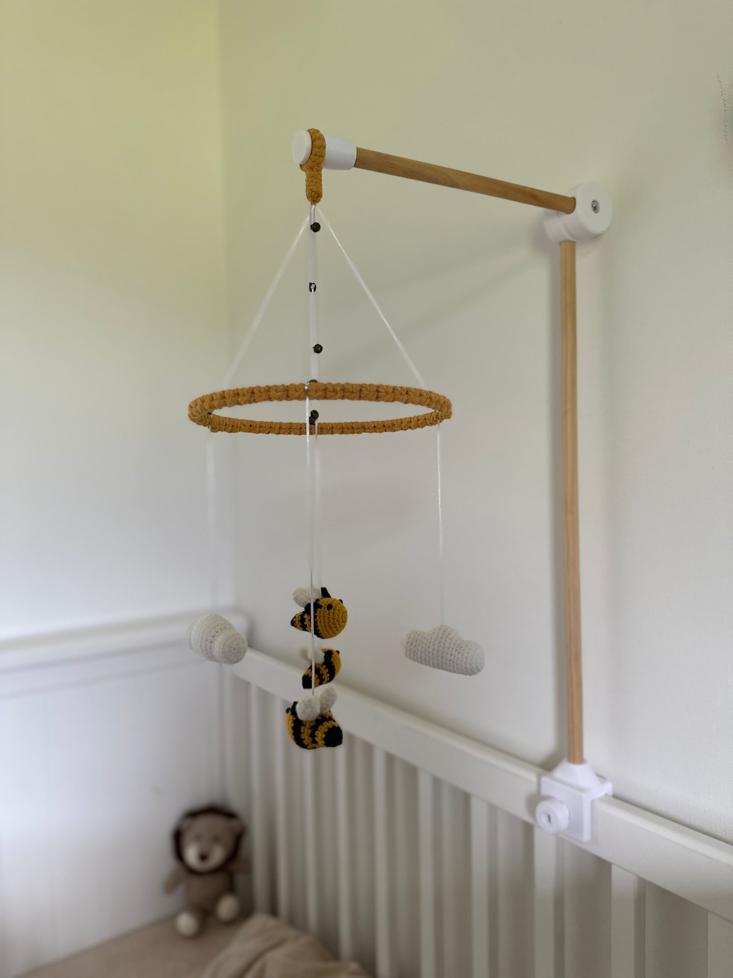 Nursery bee mobile with hanging rings and small figures hung by a wooden cot arm on a white wall.