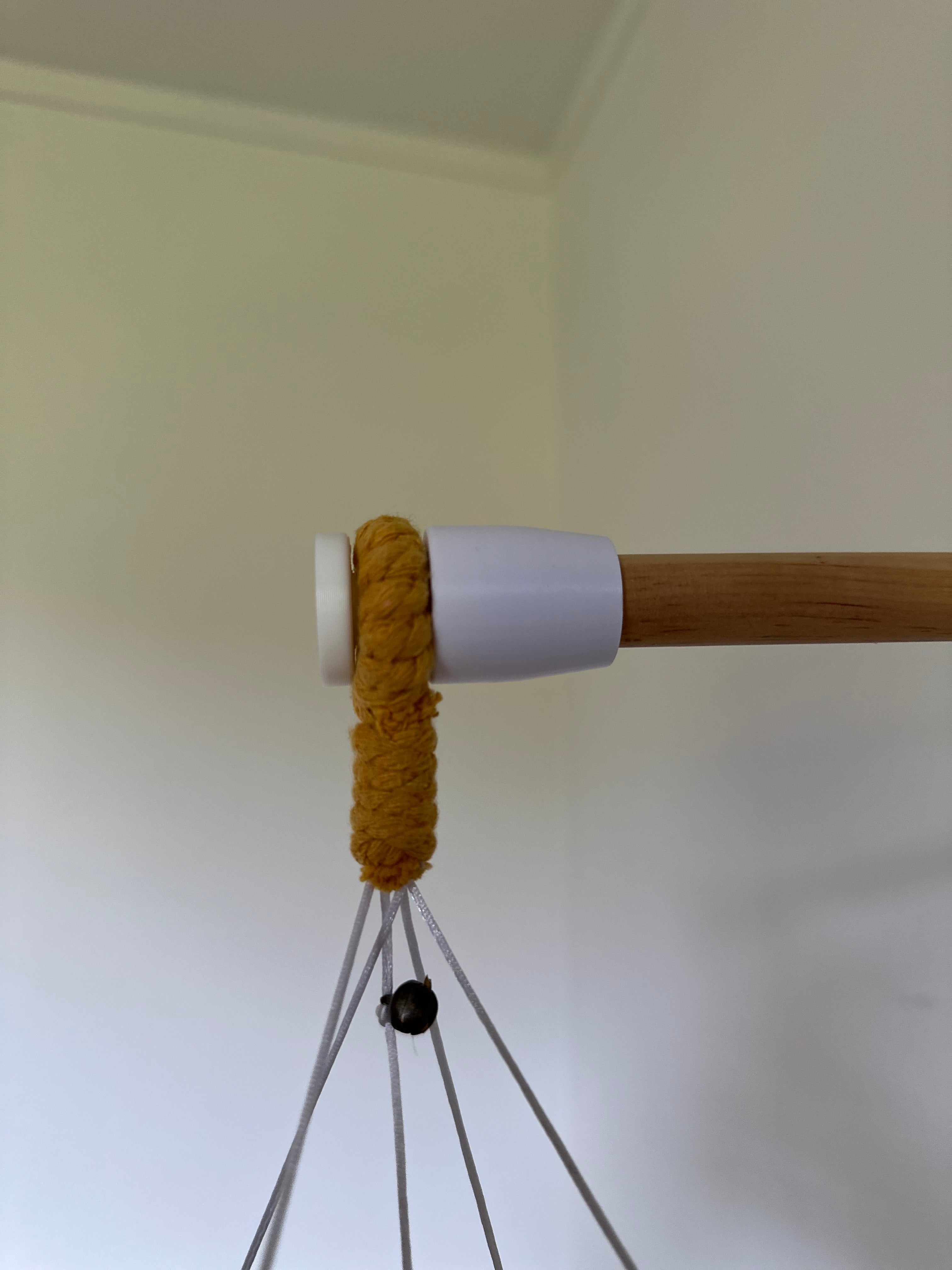 Close-up of a wooden rod with a white base and yellow macrame cord