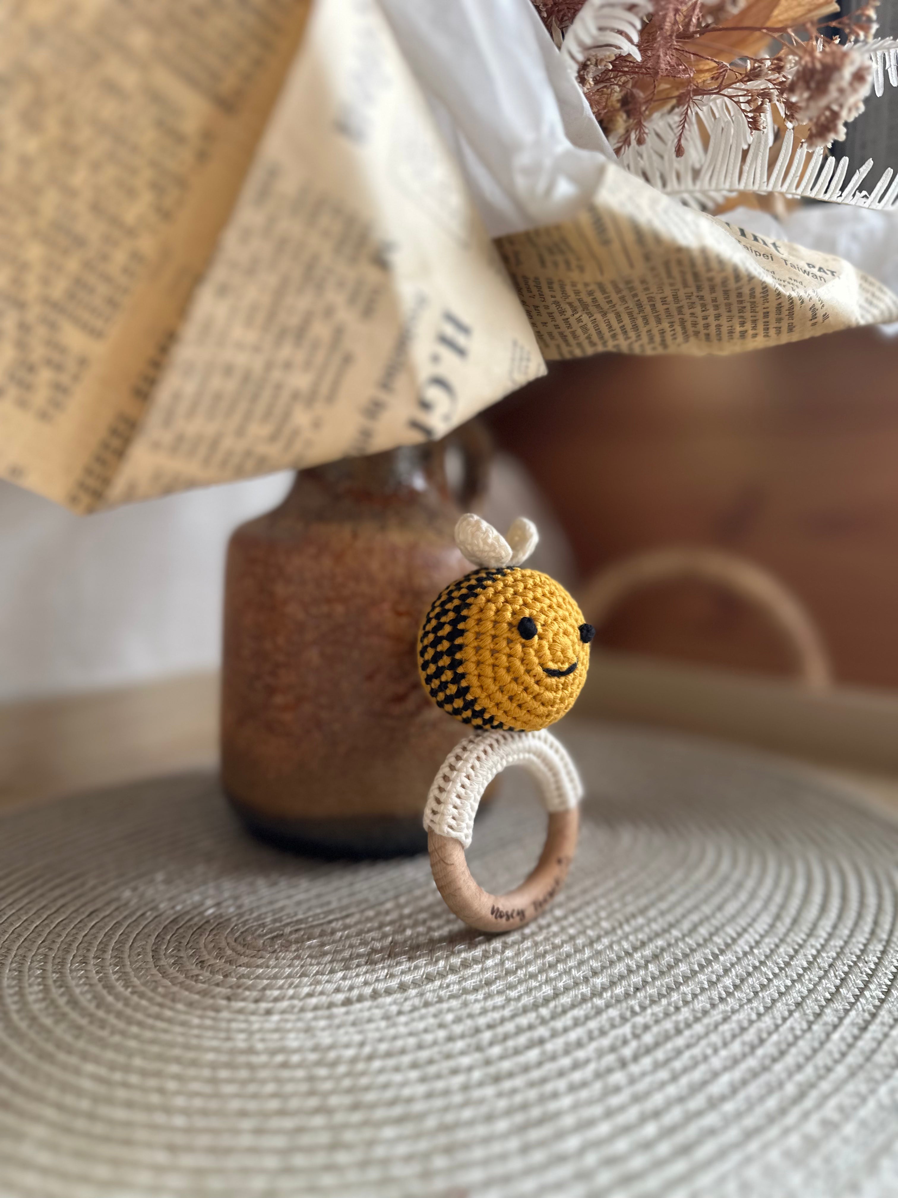 Handmade bee-shaped rattle with wooden ring on a textured surface with a blurred background