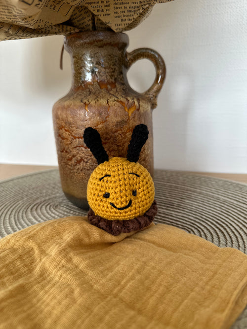 Crocheted bee toy on a mustard fabric with a ceramic jar in the background