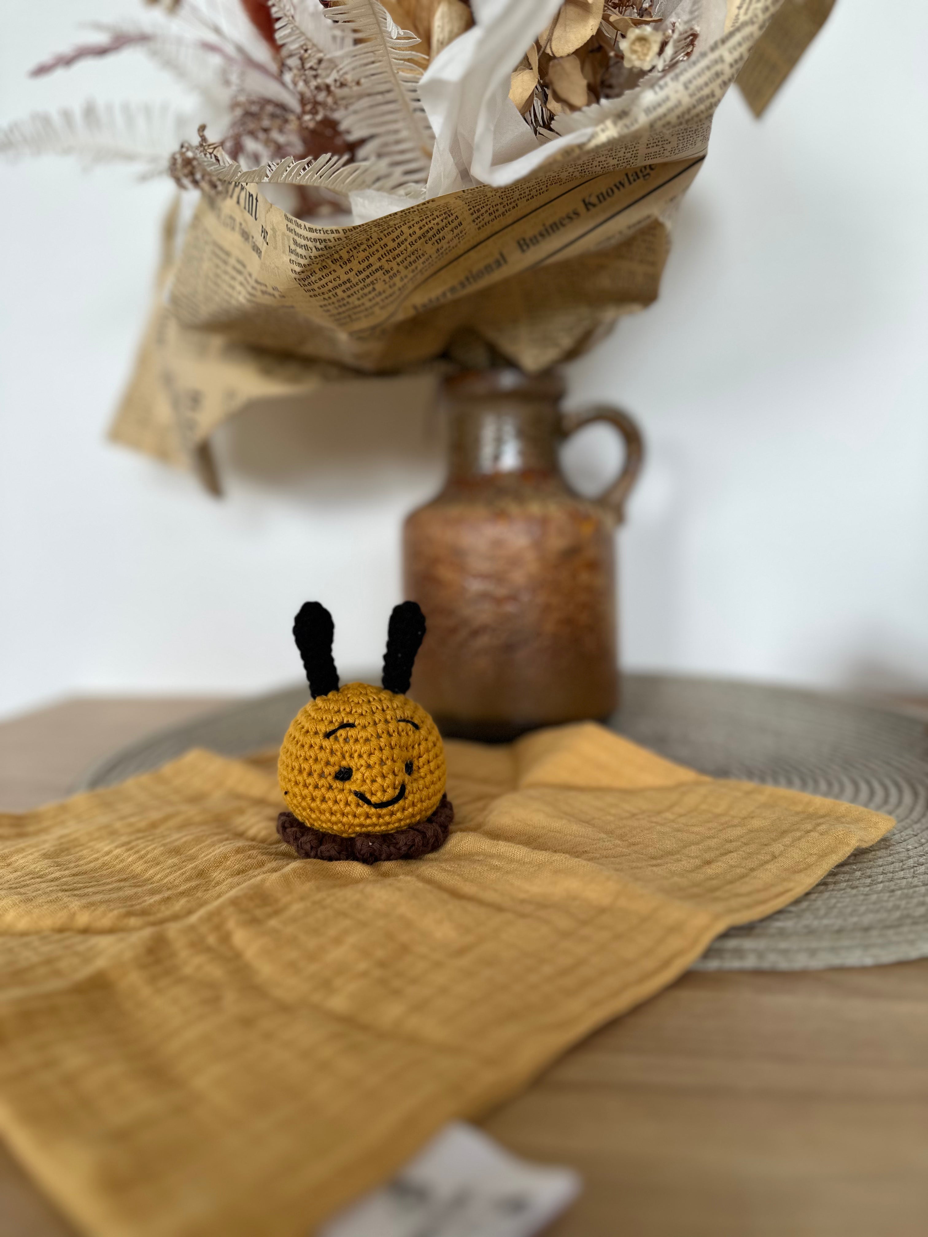 Small crocheted bee toy on a textured yellow fabric  with a rustic vase in the background.