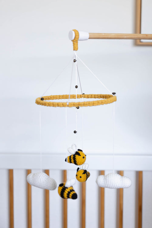 Baby crib/cot mobile with bees and clouds hanging from a wooden rod against a white background