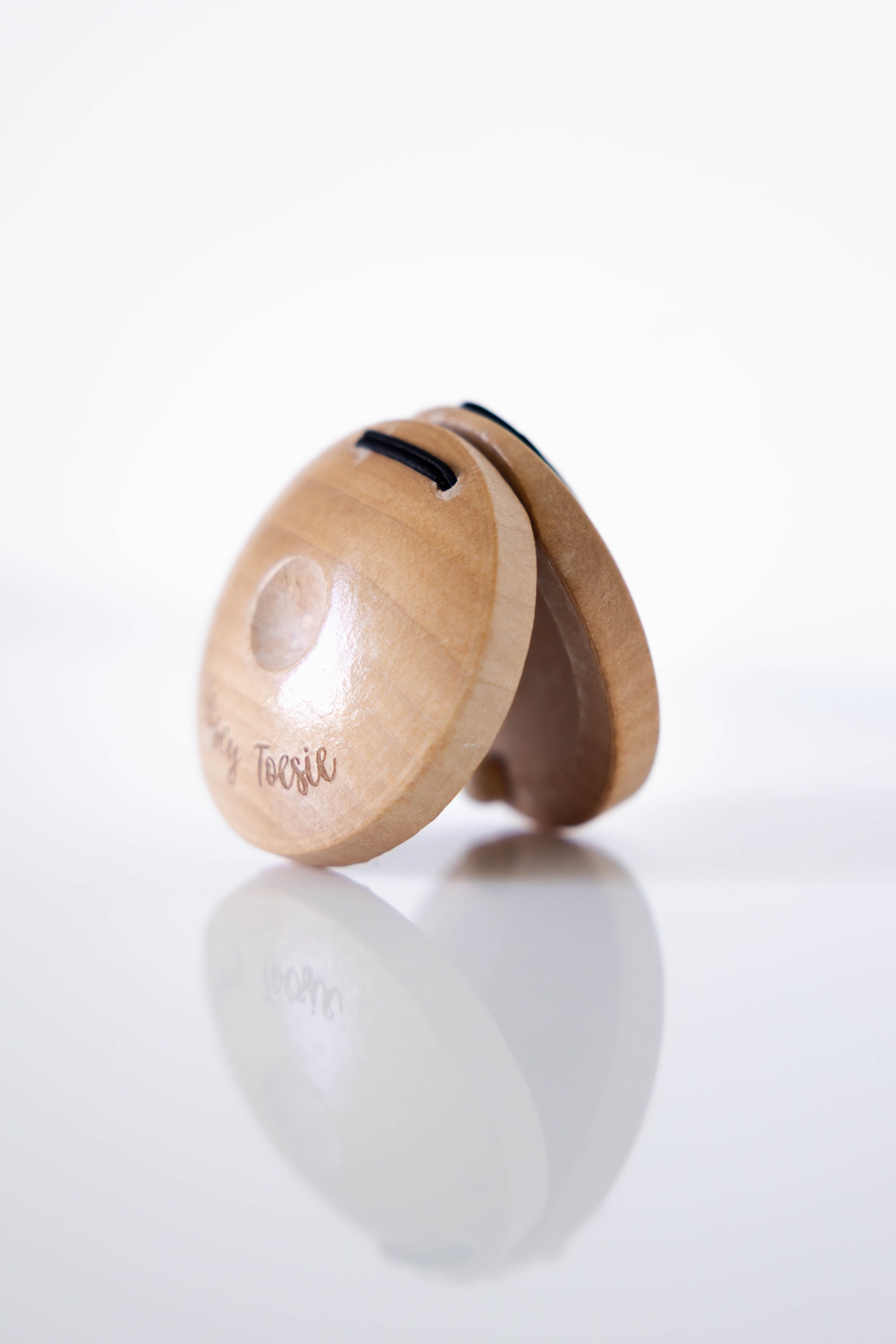 Wooden castanet instrument with a brand logo 'Nosey Toesie' on a white background