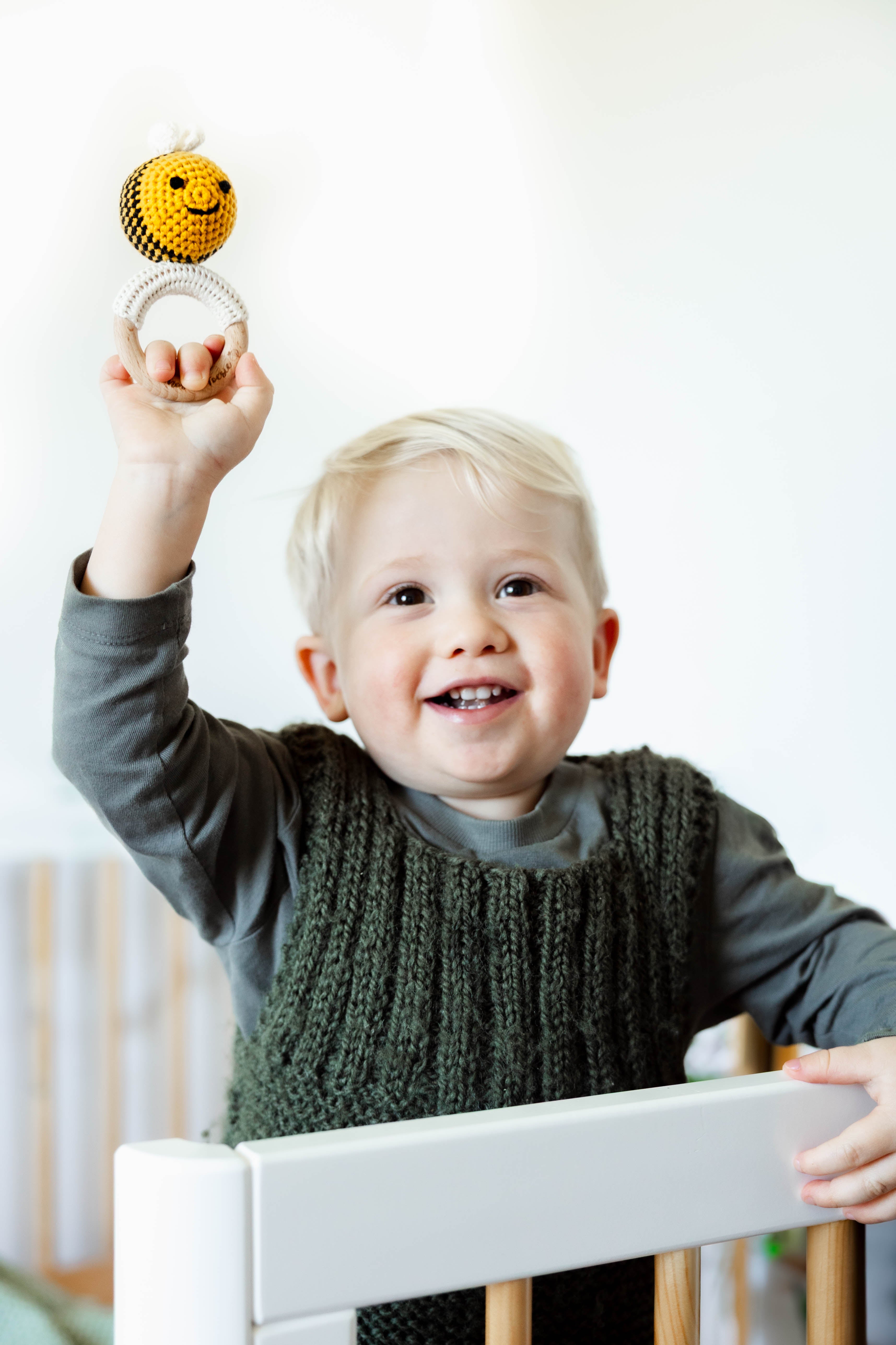Child playing with a crocheted bee with a wooden ring rattle in a crib/cot