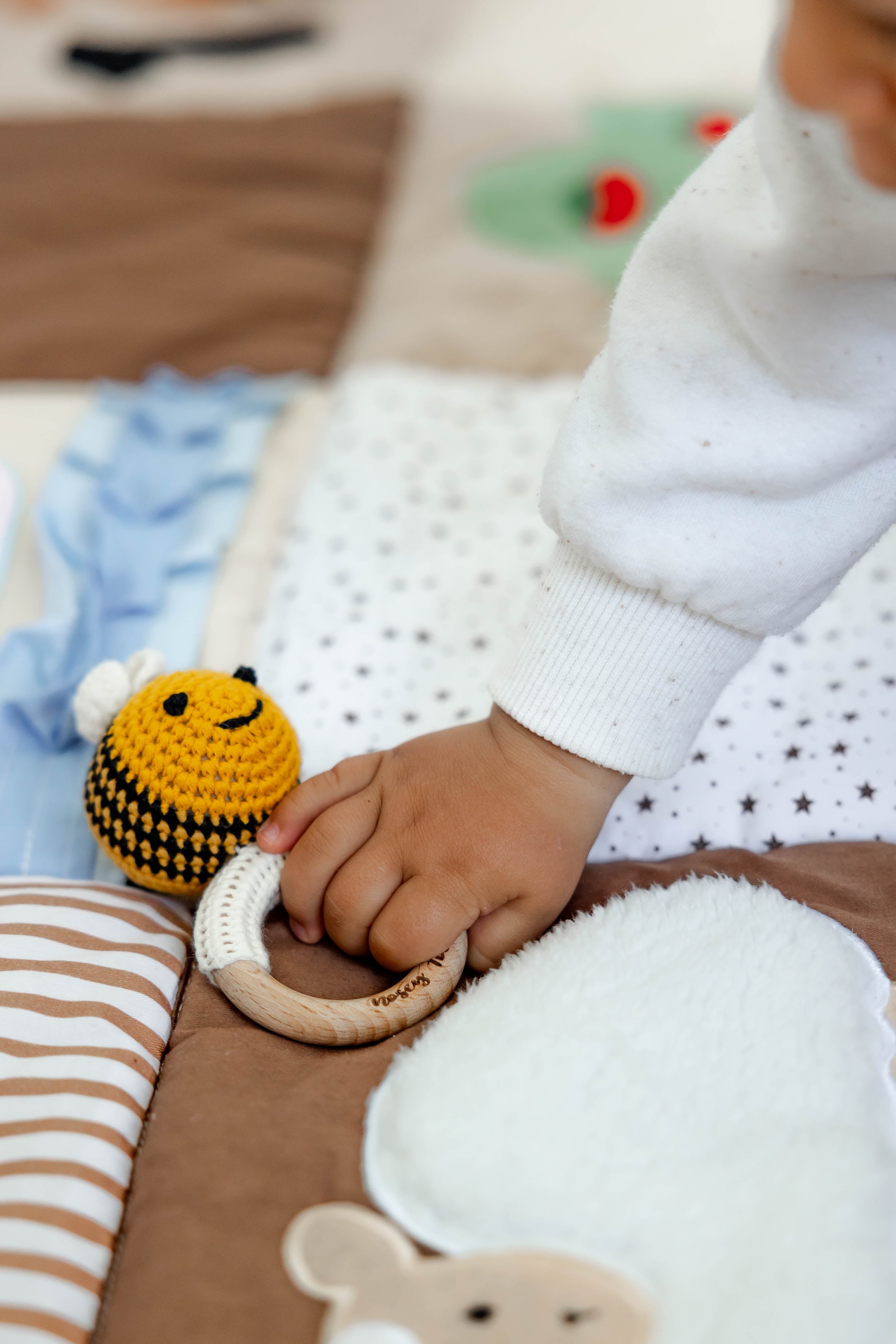 Baby hand holding a crocheted bee shaped rattle toy with a wooden ring