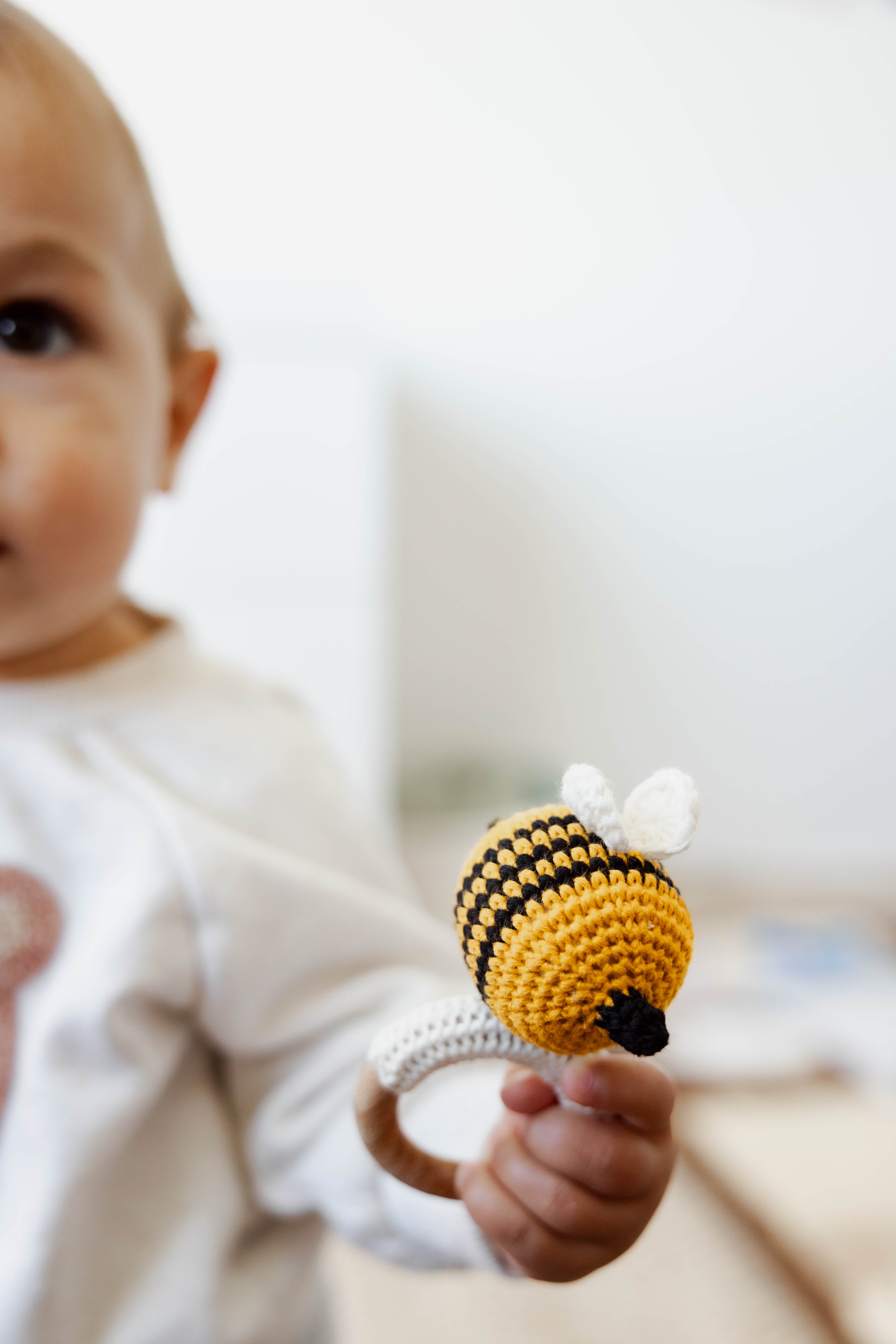 Baby holding a crocheted bee-shaped rattle toy with a blurred background