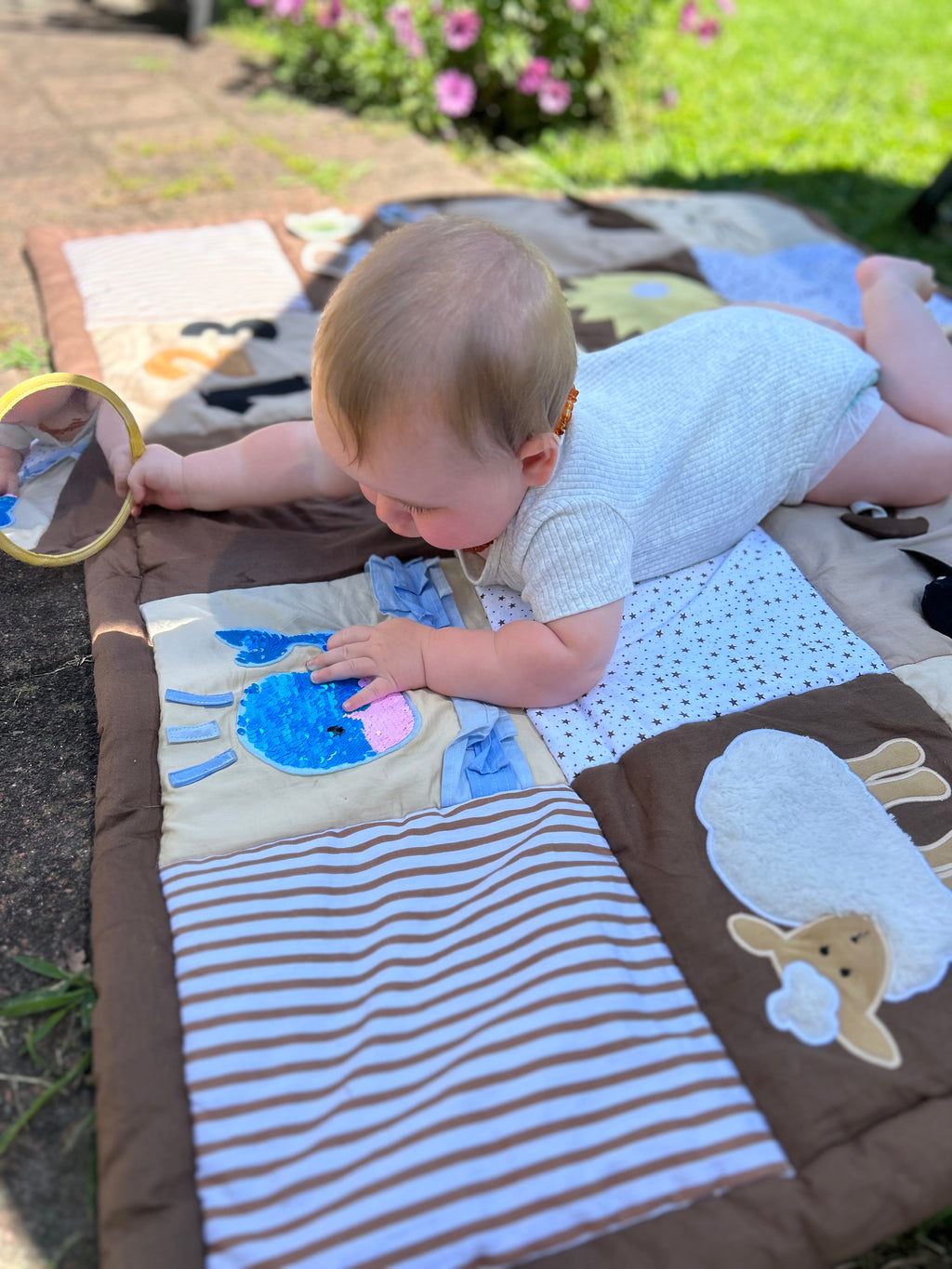 Baby playing on a colorful play mat outdoors looking at the sequined whale and holding the circle mirror