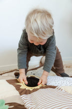 Child playing with mirror on a brown baby sensory play mat