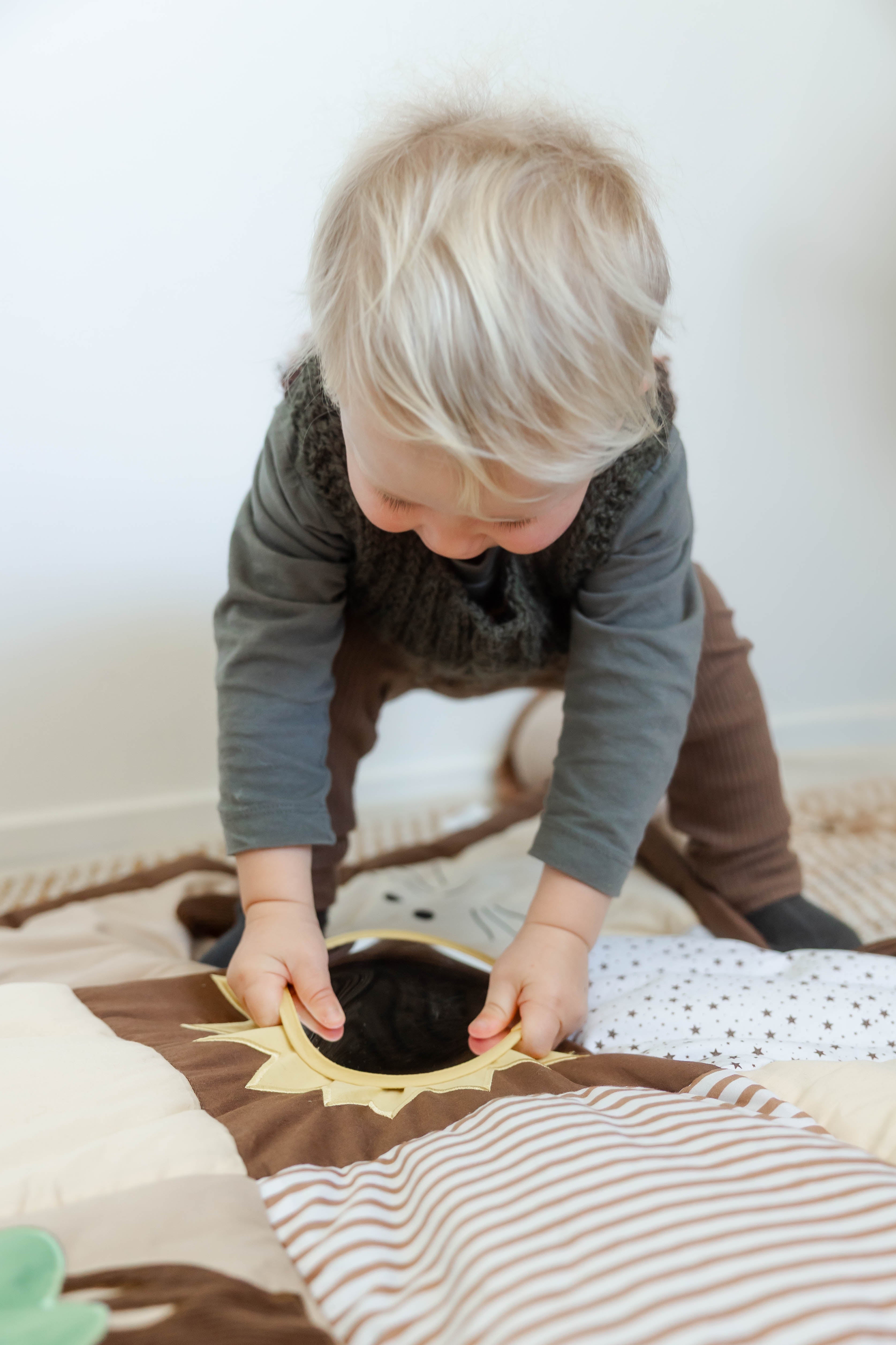 Child playing with mirror on a brown baby sensory play mat