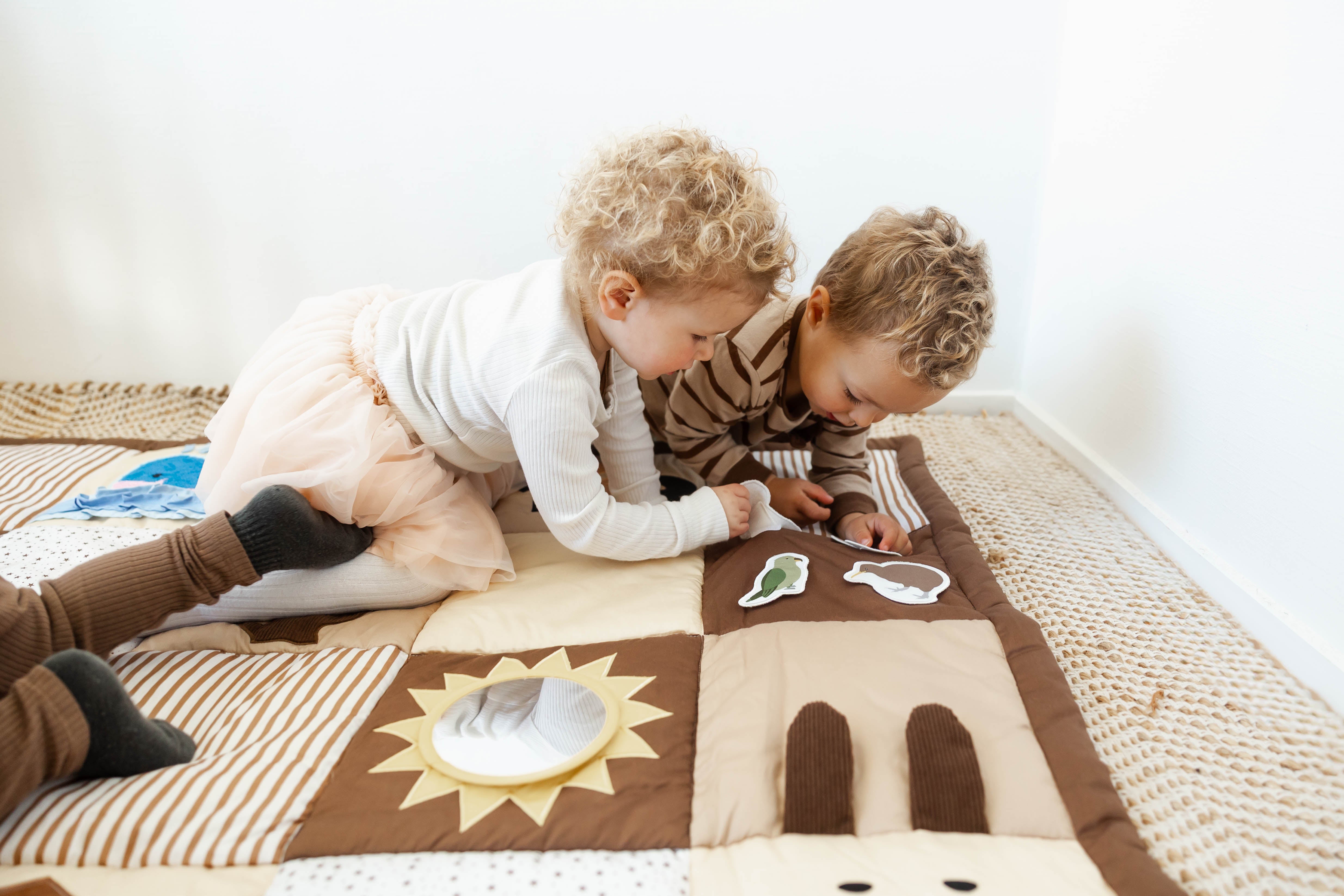 Two children playing on a patterned play mat indoors