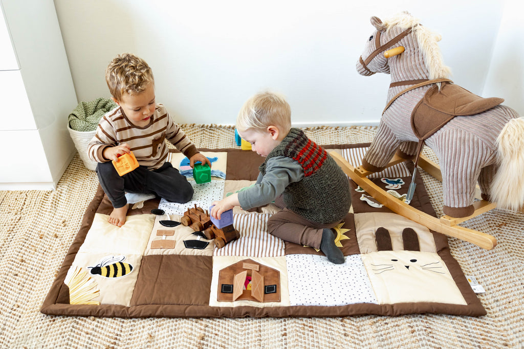 Two children playing with toys on a baby play mat in a room with a rocking horse.