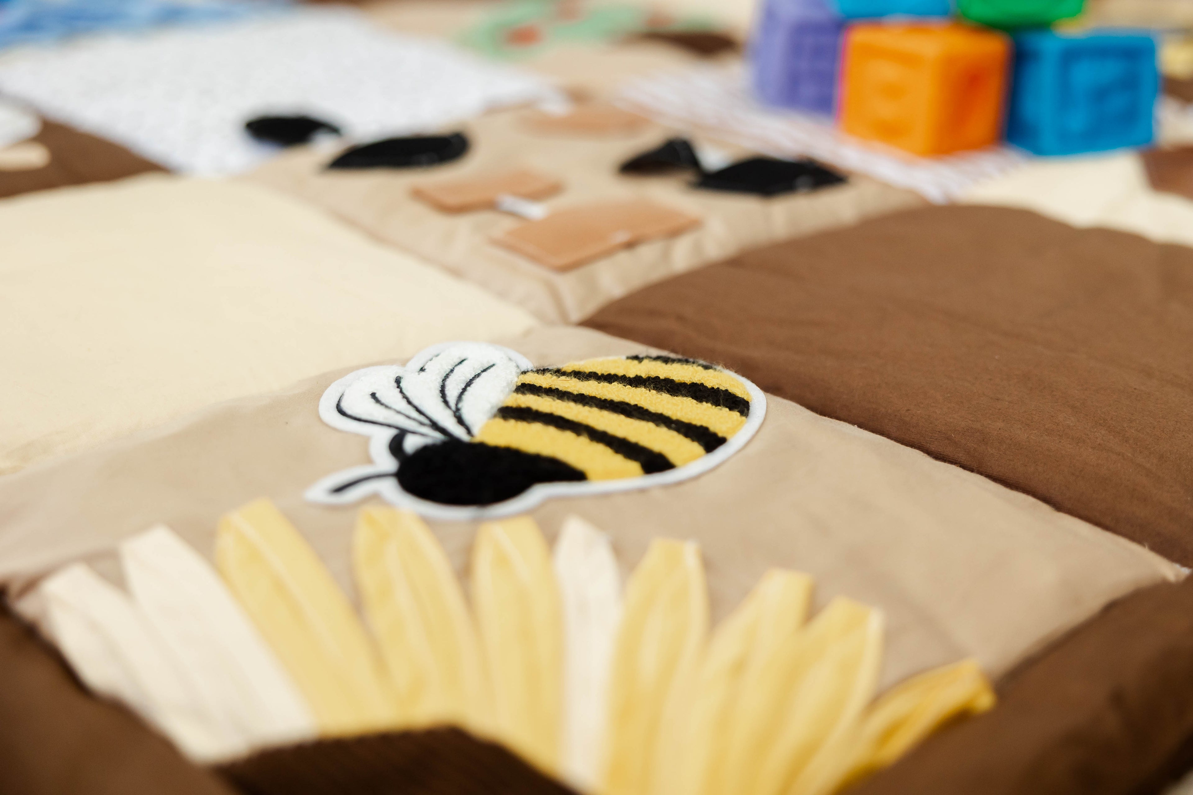 Close-up of a bee-themed children's play mat with colorful blocks in the background.