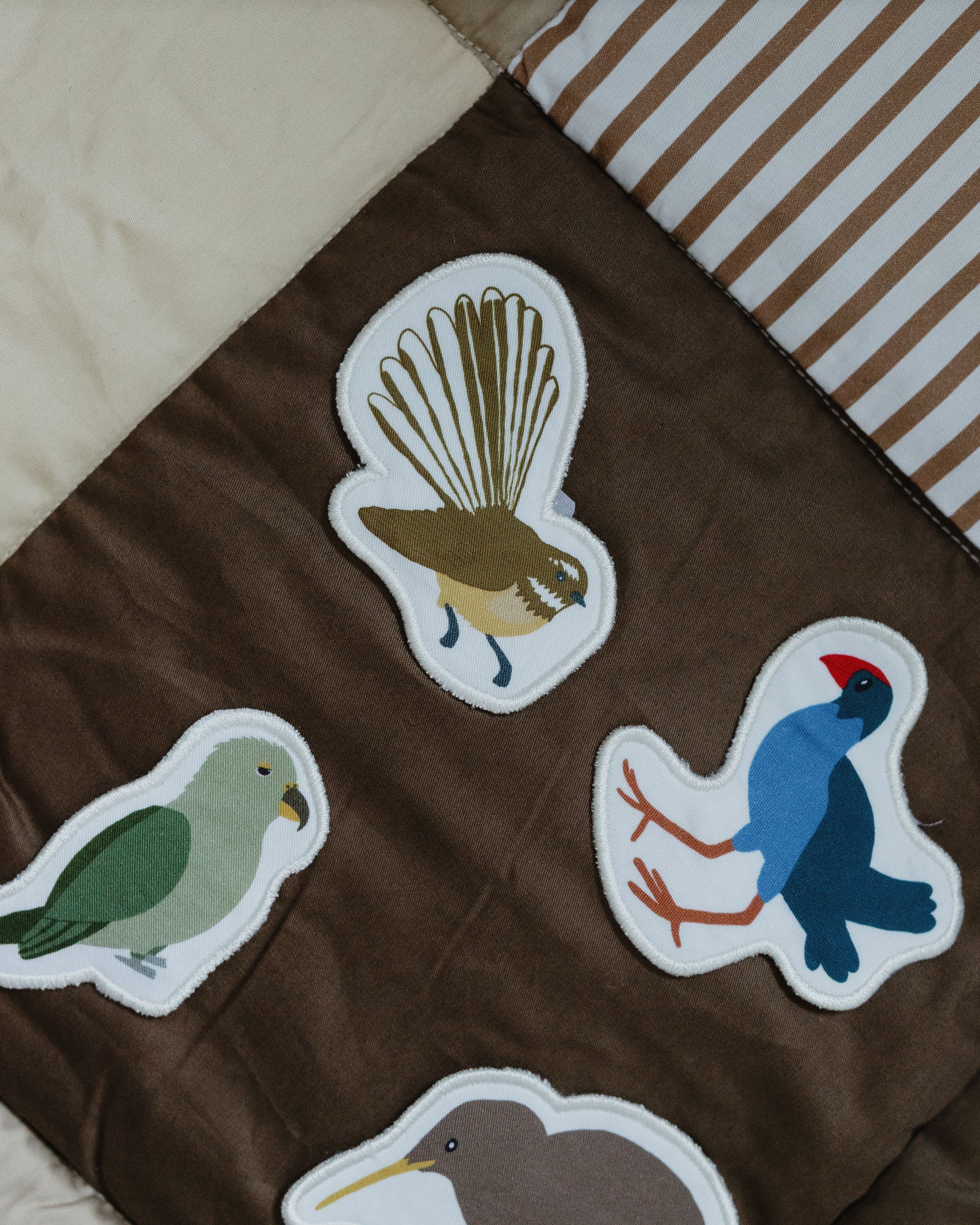 Bird-themed fabric with embroidered patches on a brown background