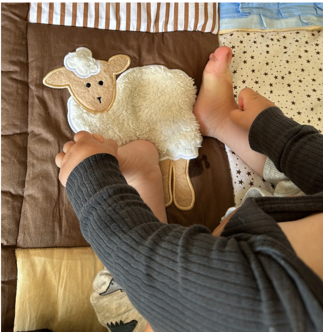 Child's hands touching a soft toy sheep design on a brown play mat